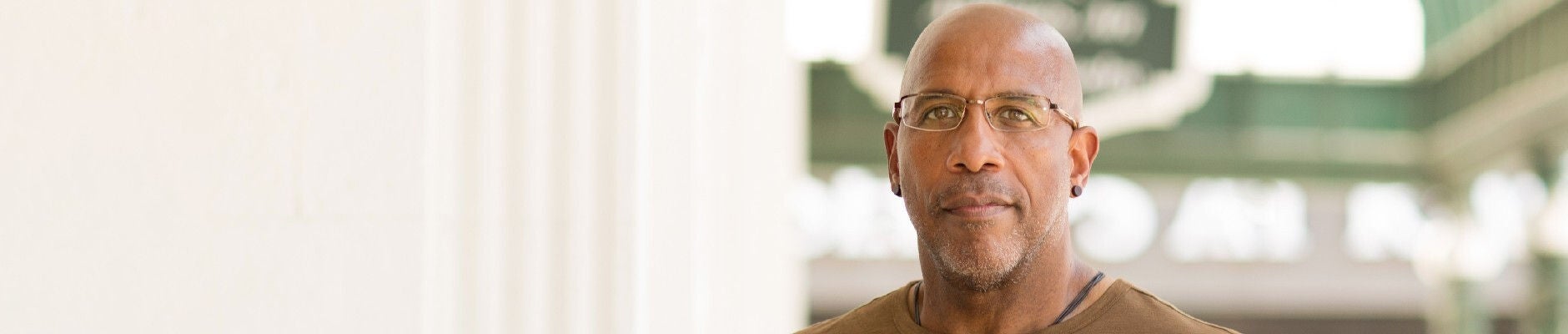 Bald, African American man wearing glasses and a brown shirt.