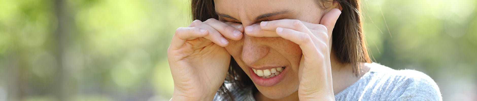 Disgusted woman rubbing her eyes standing outdoors in a park