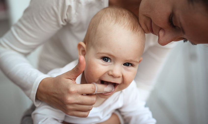 mom brushing baby teeth with finger toothbrush