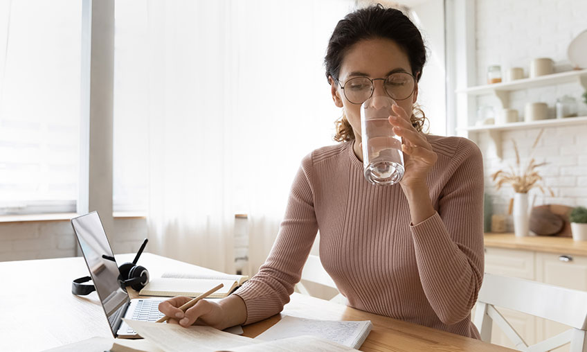 woman drinking water from glass while working from home