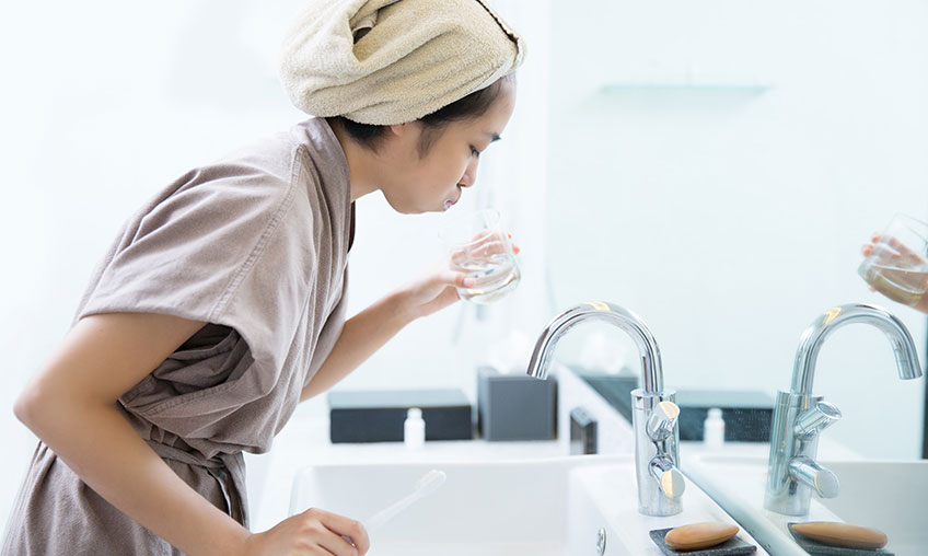 woman using mouthwash in bathroom