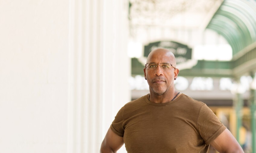 Bald, African American man wearing glasses and a brown shirt.