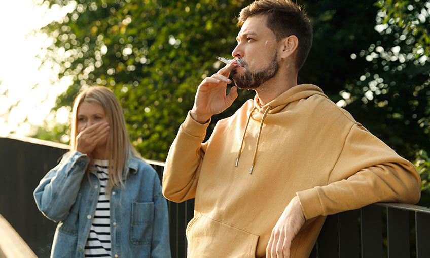 woman covering her mouth next to man smoking